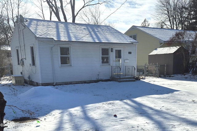 snow covered house with central AC and a shed