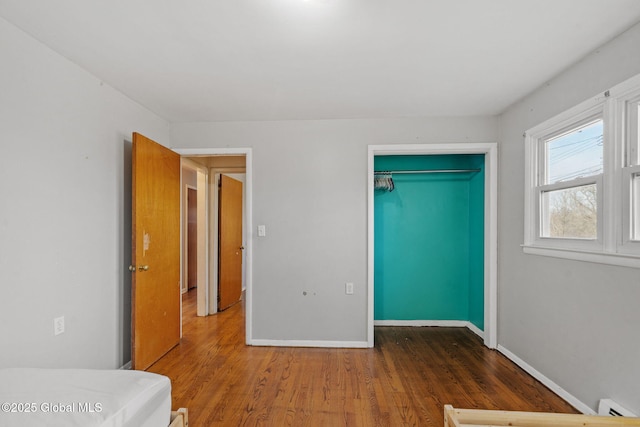 unfurnished bedroom with a closet, dark wood-type flooring, and a baseboard heating unit