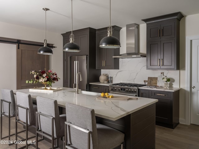 kitchen featuring wall chimney range hood, decorative light fixtures, a barn door, a large island, and premium appliances