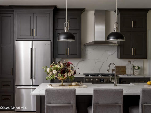 kitchen featuring pendant lighting, backsplash, wall chimney exhaust hood, light stone counters, and stainless steel refrigerator