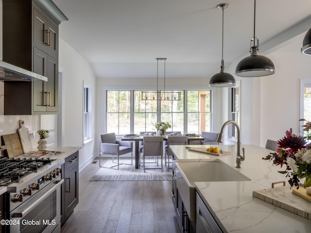 kitchen featuring wall chimney range hood, high end stainless steel range, dark hardwood / wood-style floors, light stone countertops, and decorative light fixtures