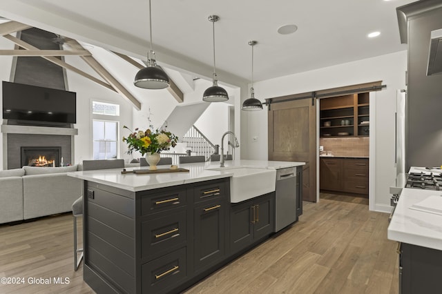 kitchen with stainless steel dishwasher, sink, a barn door, hanging light fixtures, and an island with sink