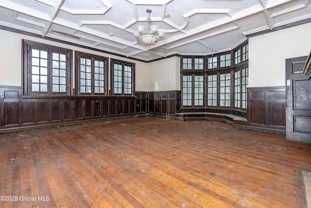 empty room with hardwood / wood-style floors, a chandelier, coffered ceiling, and ornamental molding