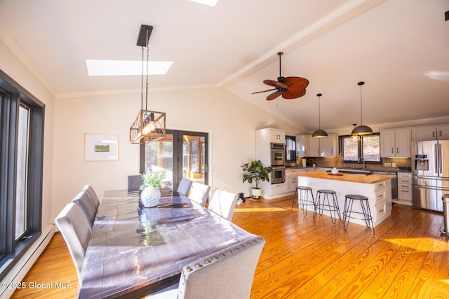 dining space featuring sink, a baseboard radiator, light hardwood / wood-style floors, and vaulted ceiling with skylight