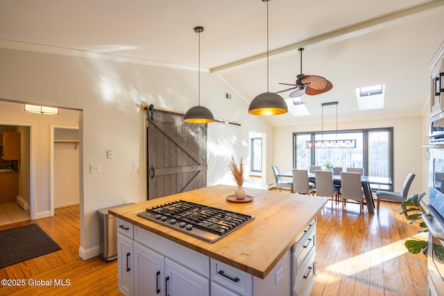 kitchen with ceiling fan, hanging light fixtures, stainless steel appliances, a barn door, and butcher block countertops