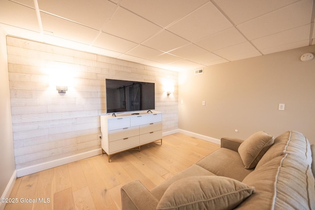 living room featuring hardwood / wood-style floors, a drop ceiling, and wood walls