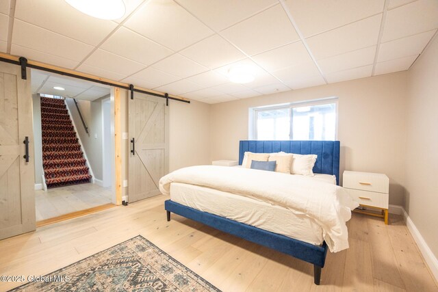 bedroom with wood-type flooring, a barn door, and a drop ceiling