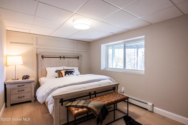 bedroom with a paneled ceiling, light hardwood / wood-style floors, and baseboard heating