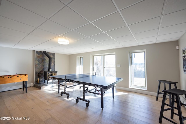 rec room featuring a wood stove, a paneled ceiling, a baseboard heating unit, and light wood-type flooring