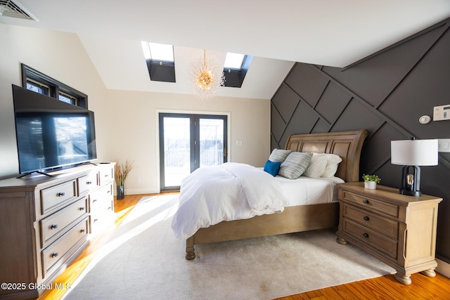 bedroom featuring a notable chandelier, access to exterior, light wood-type flooring, and lofted ceiling with skylight