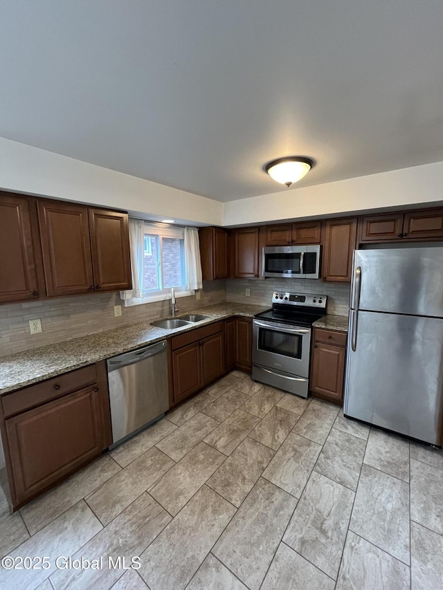 kitchen with appliances with stainless steel finishes, light stone counters, dark brown cabinets, and sink