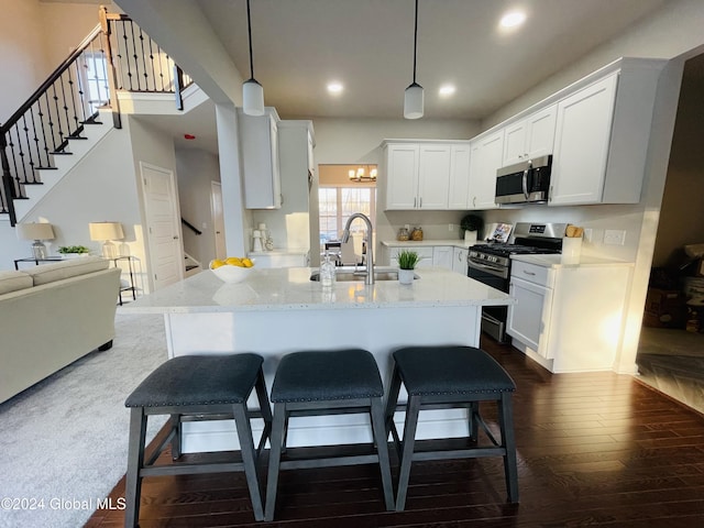 kitchen with appliances with stainless steel finishes, white cabinetry, hanging light fixtures, sink, and light stone counters