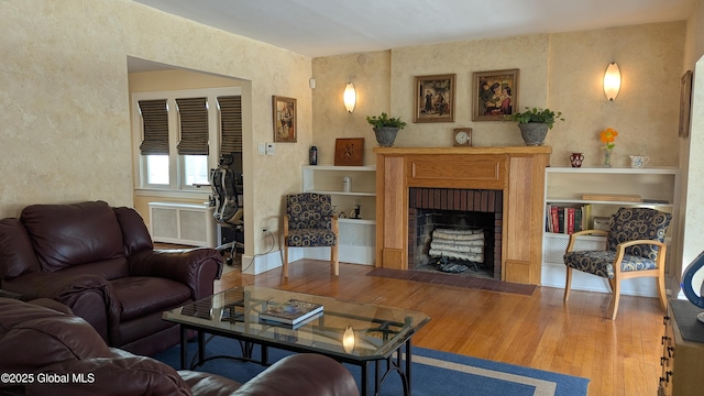 living room featuring radiator, a brick fireplace, and wood finished floors