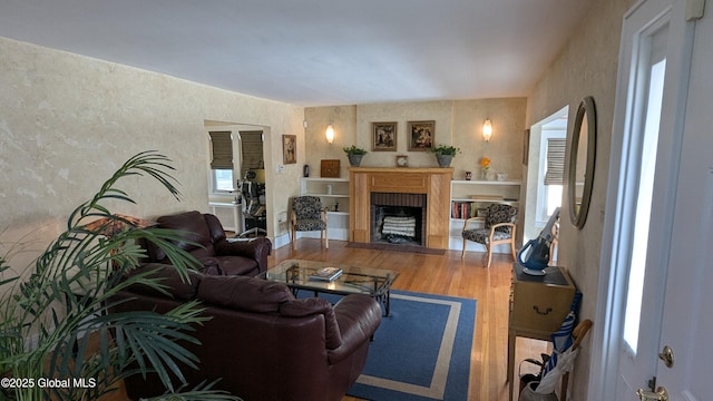 living room with a fireplace with flush hearth, wallpapered walls, and wood finished floors