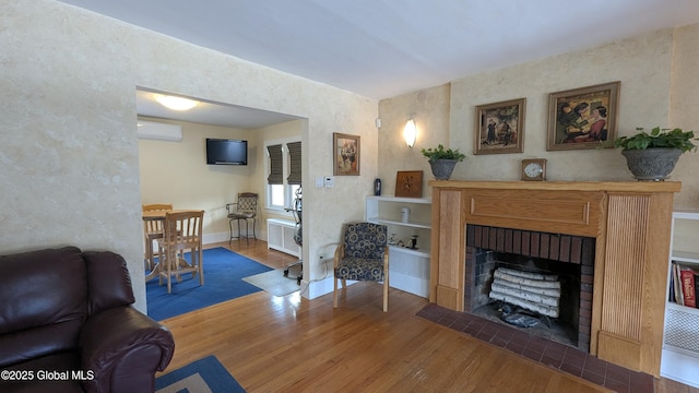 living area with a wall unit AC, radiator heating unit, a fireplace, and wood finished floors