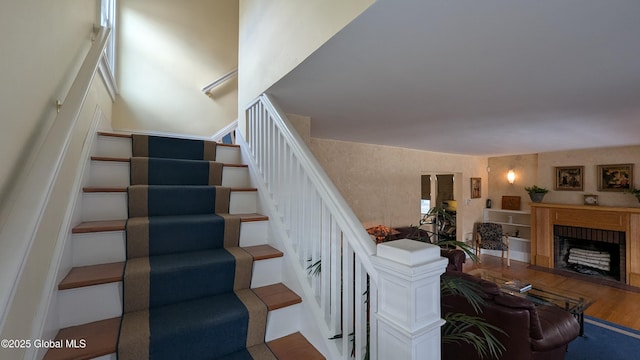 stairs featuring a fireplace with flush hearth and wood finished floors