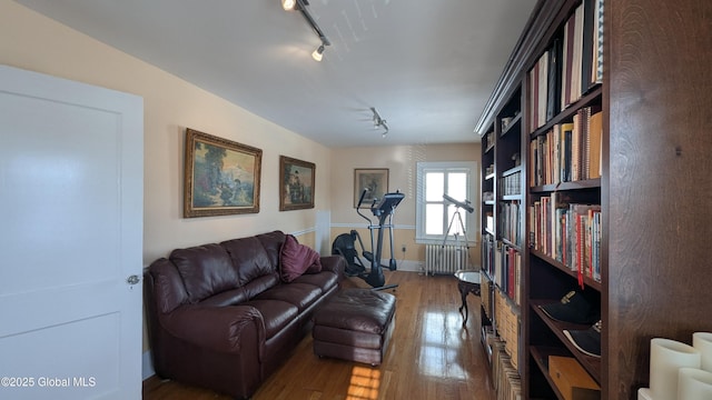 living area with radiator, track lighting, and wood finished floors