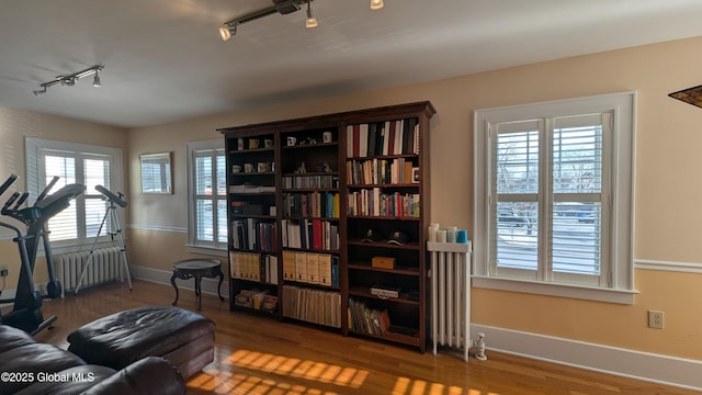 living area featuring radiator heating unit, wood finished floors, rail lighting, and baseboards