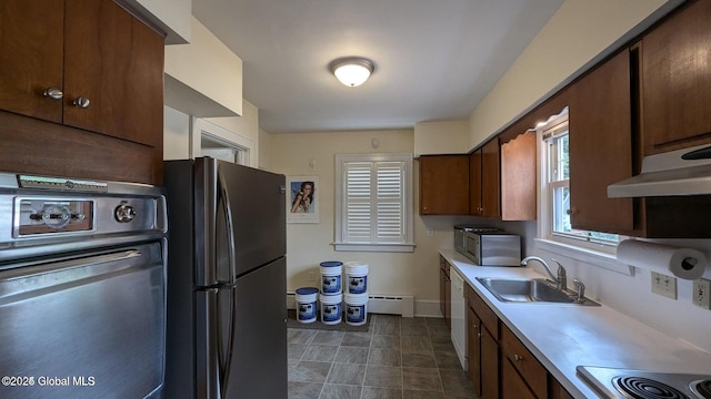 kitchen with light countertops, baseboard heating, appliances with stainless steel finishes, a sink, and baseboards