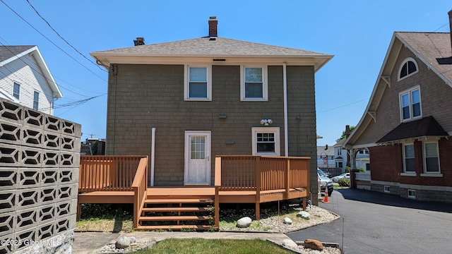 back of house featuring aphalt driveway, a shingled roof, a chimney, and a wooden deck