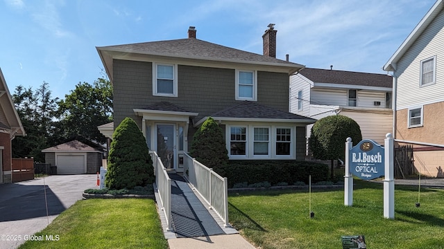 view of front facade with a garage, roof with shingles, a front lawn, and an outdoor structure