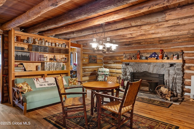 dining space featuring rustic walls, a fireplace, beam ceiling, hardwood / wood-style flooring, and a chandelier