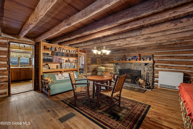 dining space featuring rustic walls, wood ceiling, beamed ceiling, a chandelier, and a stone fireplace