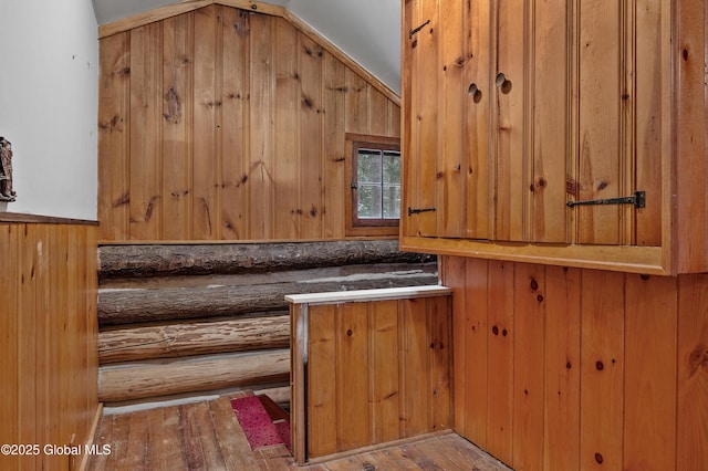 interior space featuring light wood-type flooring, rustic walls, vaulted ceiling, and wood walls