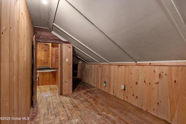 additional living space with wood-type flooring, lofted ceiling, and wooden walls