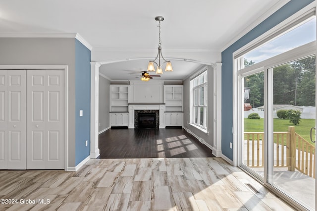 unfurnished living room with wood-type flooring, ceiling fan with notable chandelier, ornate columns, and crown molding