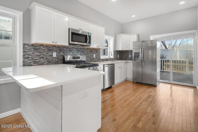 kitchen featuring white cabinets, sink, light wood-type flooring, kitchen peninsula, and stainless steel appliances