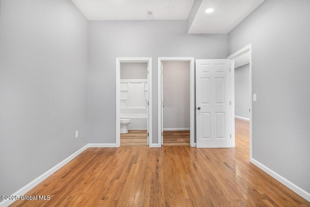 unfurnished bedroom with ensuite bath, a spacious closet, and light wood-type flooring