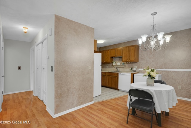 kitchen with decorative light fixtures, an inviting chandelier, white appliances, and light hardwood / wood-style flooring