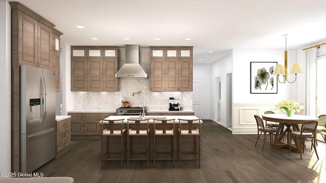 kitchen with dark hardwood / wood-style floors, wall chimney range hood, an inviting chandelier, an island with sink, and stainless steel fridge