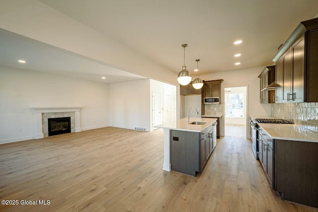 kitchen featuring stainless steel appliances, decorative backsplash, sink, hanging light fixtures, and a kitchen island with sink