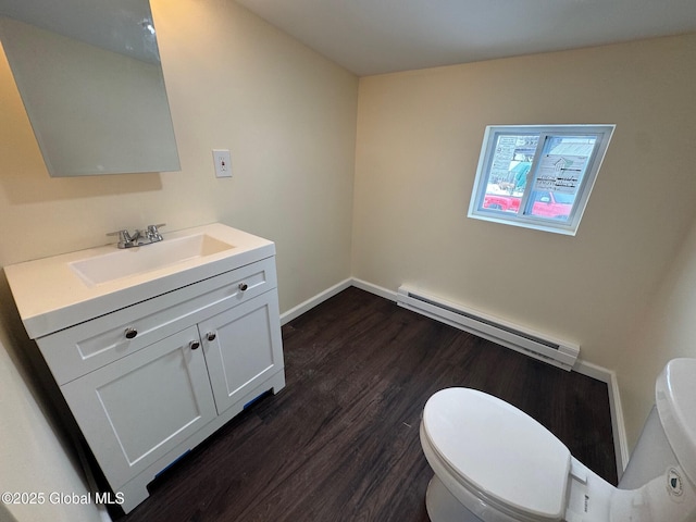 half bath with toilet, a baseboard heating unit, vanity, wood finished floors, and baseboards