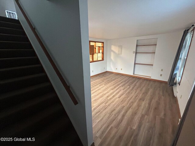 unfurnished living room featuring visible vents, baseboards, wood finished floors, and stairs