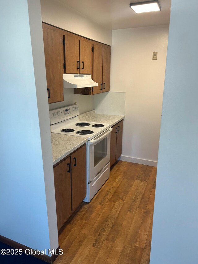 kitchen featuring under cabinet range hood, hardwood / wood-style floors, white electric range oven, light countertops, and baseboards