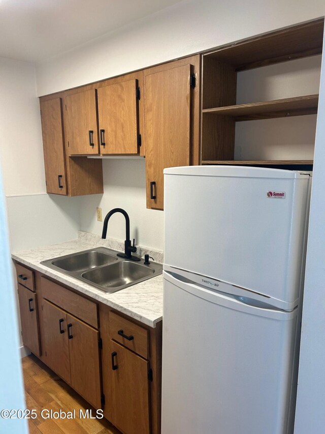 kitchen with a sink, light countertops, freestanding refrigerator, light wood-style floors, and open shelves