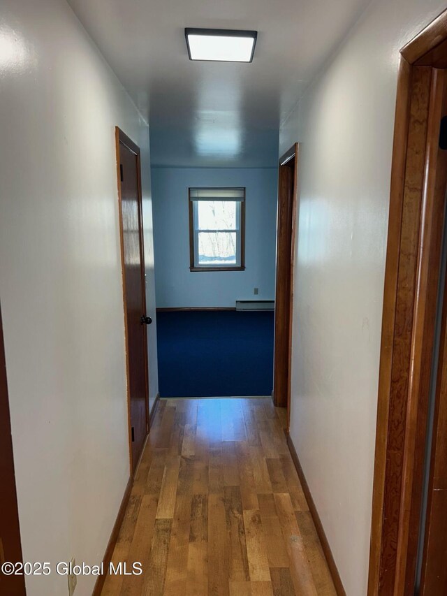 corridor featuring baseboard heating, baseboards, and hardwood / wood-style flooring