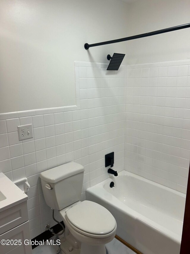 bathroom featuring vanity, wainscoting, shower / washtub combination, tile walls, and toilet