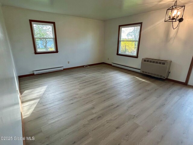 empty room with a notable chandelier, baseboard heating, and wood finished floors