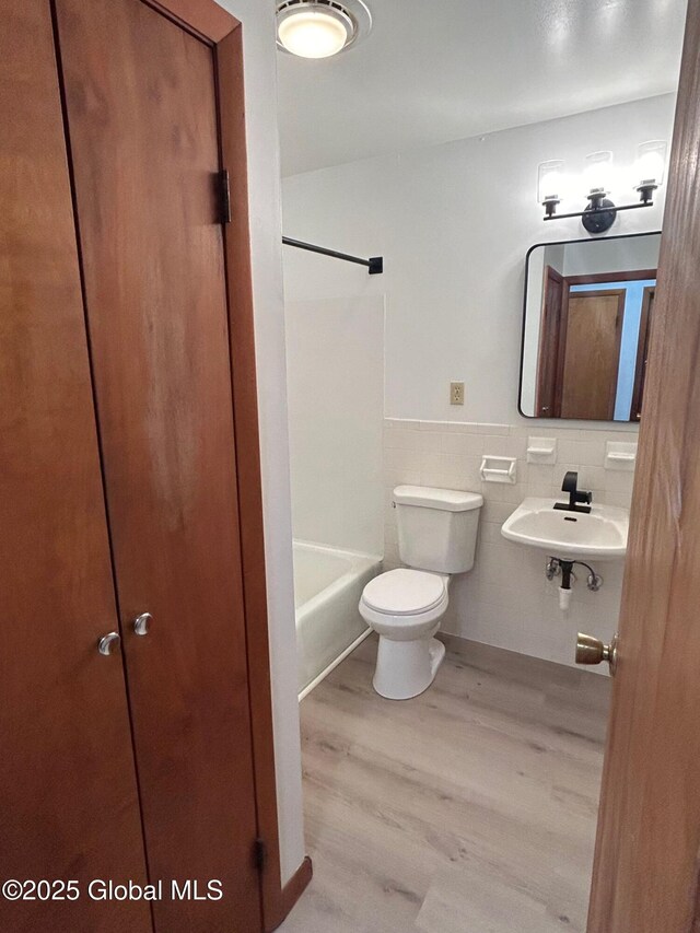 bathroom with a wainscoted wall, toilet, wood finished floors, tile walls, and a sink