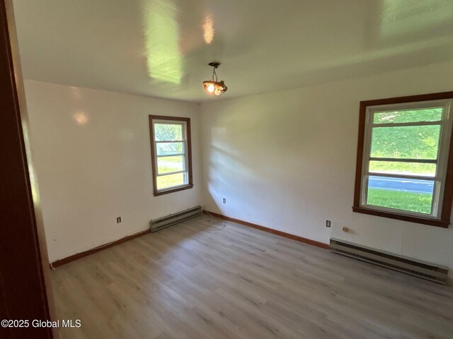 unfurnished room featuring a baseboard heating unit, baseboards, and light wood-style flooring