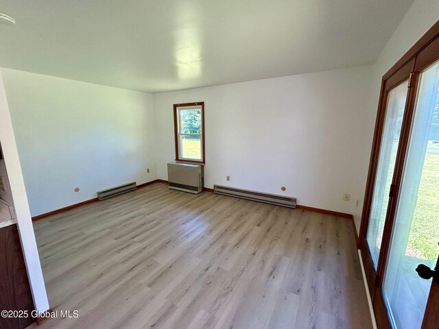 empty room featuring a baseboard heating unit, baseboards, and light wood finished floors