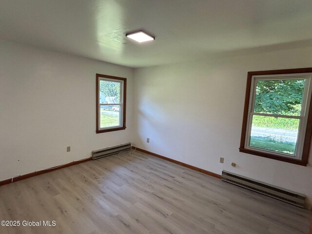 spare room featuring a baseboard heating unit, baseboards, and light wood-style flooring