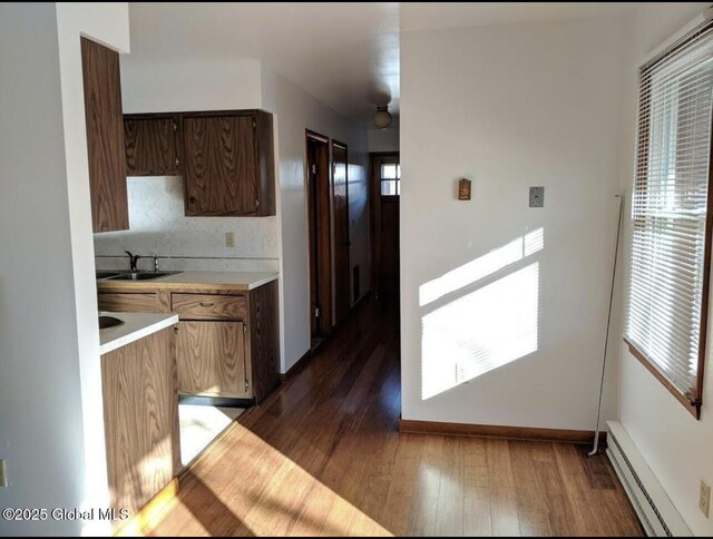 kitchen with dark wood-type flooring, a sink, tasteful backsplash, light countertops, and baseboard heating