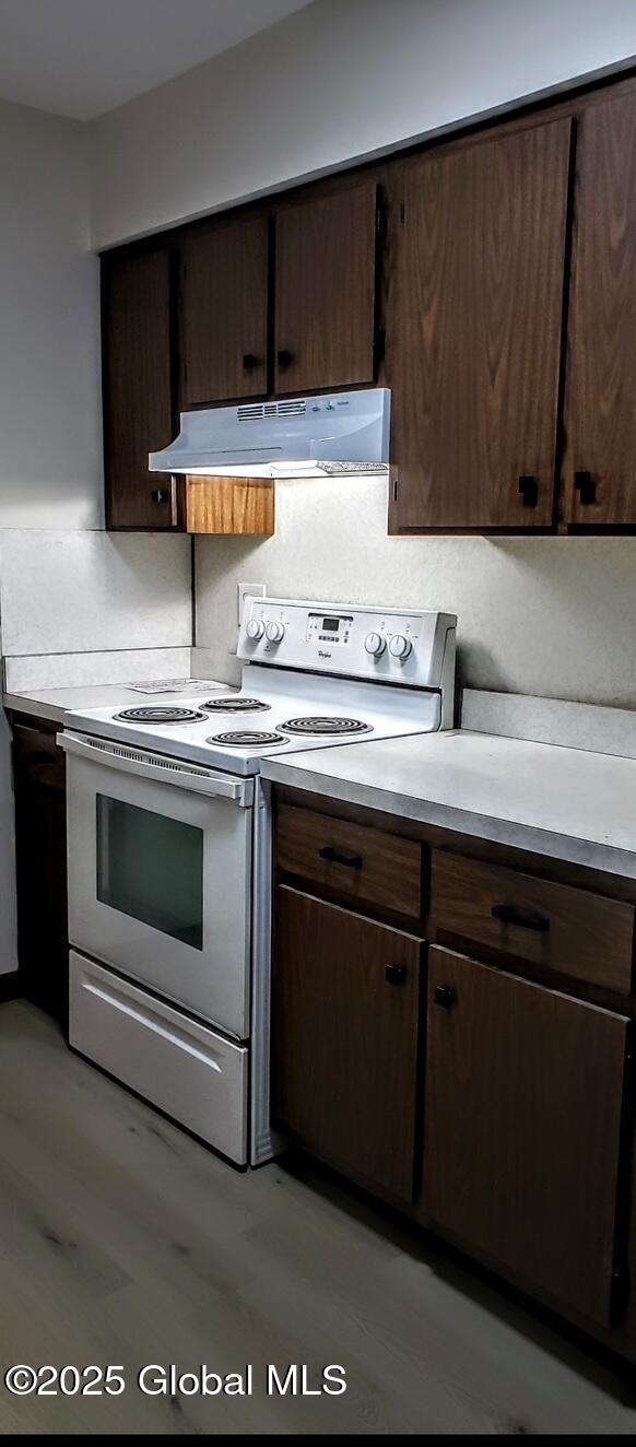 kitchen featuring dark brown cabinetry, light countertops, under cabinet range hood, and white range with electric stovetop