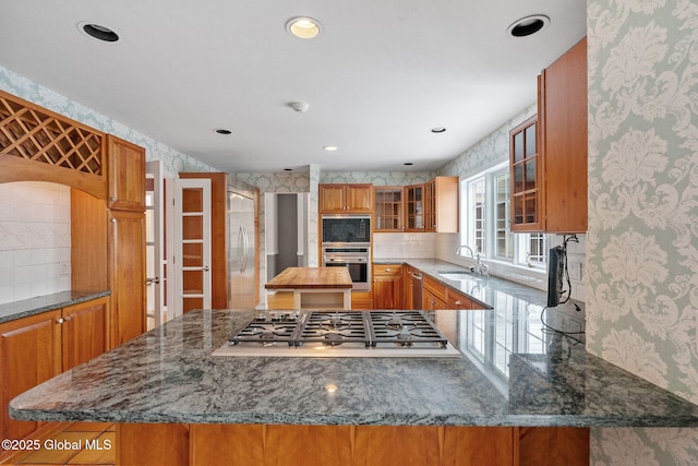 kitchen featuring stainless steel appliances, dark stone counters, tasteful backsplash, sink, and kitchen peninsula