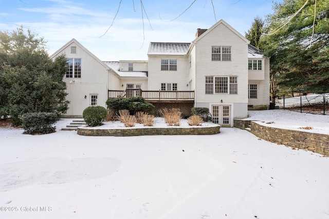 snow covered back of property featuring french doors and a wooden deck